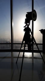 Silhouette of camera against sky seen through glass window