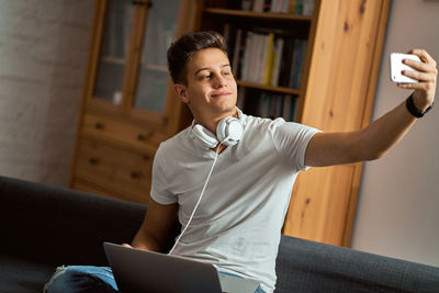 Man with headphones taking selfie while sitting on sofa at home