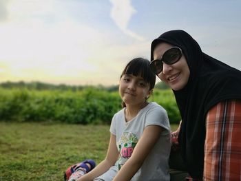 Portrait of smiling mother and daughter sitting on field during sunset