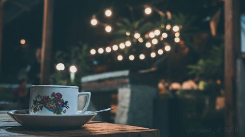 Close-up of coffee cup on table against illuminated lights at night