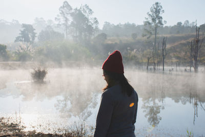 Side view of woman standing by lake against trees