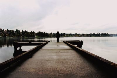 Rear view of silhouette man standing on lake against sky