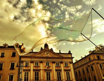 Large soap bubble in front of building against sky during sunset
