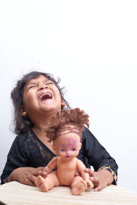 Happy girl playing with doll while sitting against white background