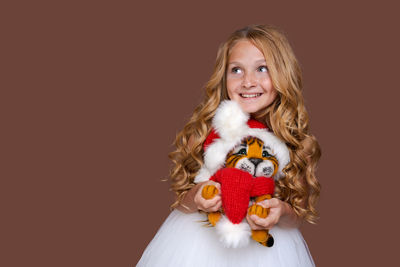 Child plays with cute little christmas tiger toy in white dress on brown