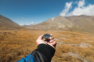 Pov male traveler's hand holding a magnetic compass against the backdrop of a mountainous area. 