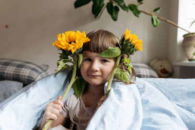 Portrait of a toddler girl holding sunflowers and looking at the camera