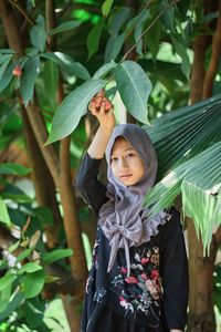 Portrait of young woman standing against plants