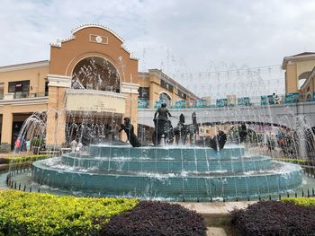 Fountain by building against sky in city