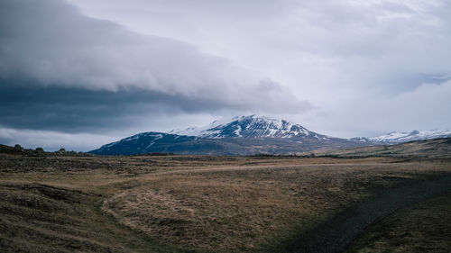 Scenic view of landscape and snowcapped mountains against cloudy sky