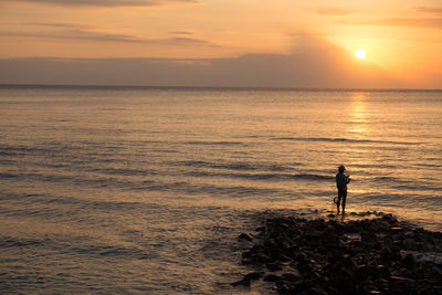 Silhouette man standing on sea against sky during sunset