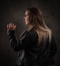 Side view of young woman standing against black background