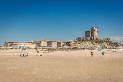 People at beach against clear blue sky