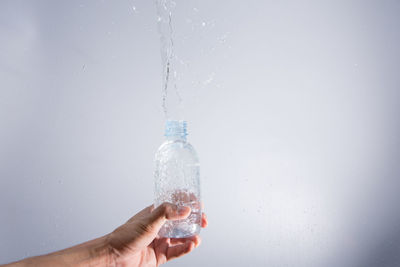 Close-up of hand holding bottle against white background