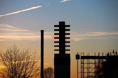 Silhouette factory against sky during sunset