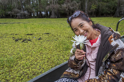 Portrait of smiling senior woman holding flower while sitting on boat