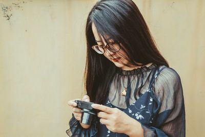 Young woman using camera against wall