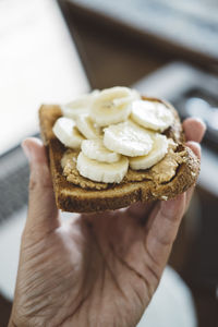 Cropped hand of man holding bread with banana slices at home