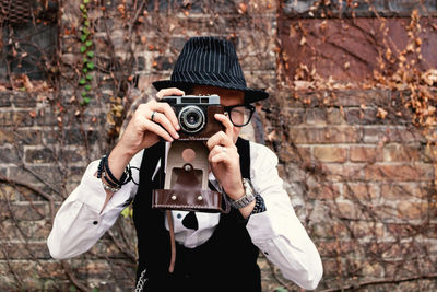 Retro-styled man photographing with analog photo camera outdoors.