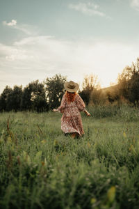 Rear view of woman standing on grassy field against sky