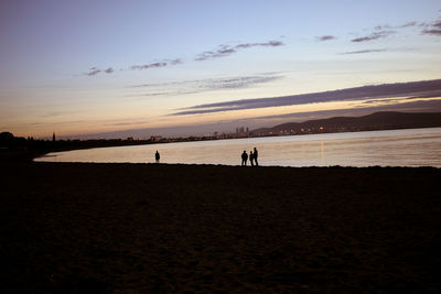 Silhouette people on beach against sky during sunset