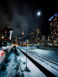 Illuminated street amidst buildings against sky during winter toronto cn tower