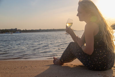 Side view of woman drinking glass at beach