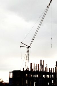 Low angle view of silhouette crane by building against sky during sunset