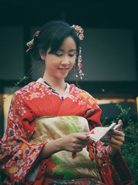 Smiling teenage girl wearing kimono looking away against house