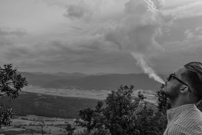 Young man exhaling smoke against sky