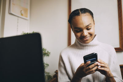 Smiling teenage girl using mobile phone while sitting at home