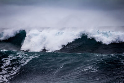 Waves splashing on shore against sky