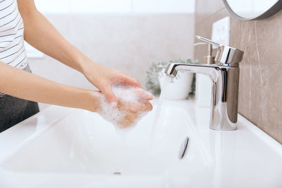 Cropped hands washing faucet in sink in bathroom