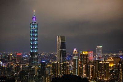 Illuminated modern buildings in city against sky at night