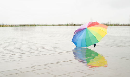 Unused colorful umbrella lying on ground being rained upon. rainbow colored umbrella