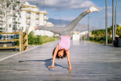 Full length of woman practicing cartwheel on footpath in city