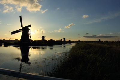 River by silhouette traditional windmills against sky during sunset