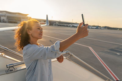 Portrait of smiling young woman taking selfie while standing in city