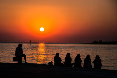 Silhouette people sitting at beach against sky during sunset