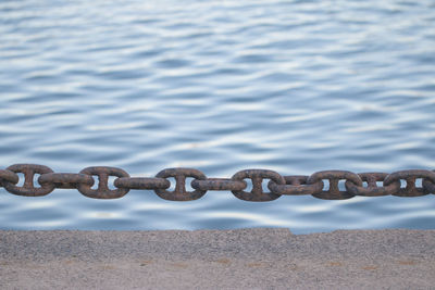 Close-up of rusty chain against river 