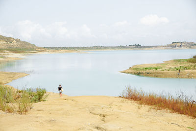 Rear view of woman standing on beach against sky