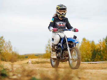 Young woman with curly hair in protective gear riding on a motorcycle with autumn backstage