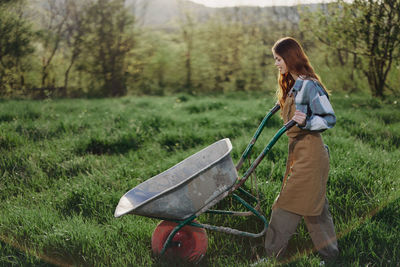 Side view of woman walking on grass with wheelbarrow