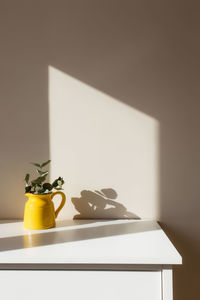 A yellow ceramic jug or vase with eucalyptus branches, empty white photo frames on the white table