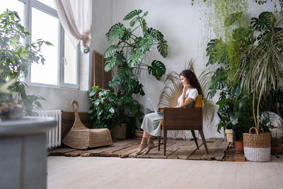 Joyful woman with laptop on knees in harmony with plants around feeling relax comfort at cozy home.