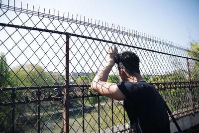 Rear view of person standing by chainlink fence against sky