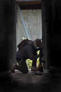 Young man holding rifle wearing mask kneeling in corridor