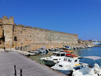 Boats moored at harbor by buildings against clear blue sky