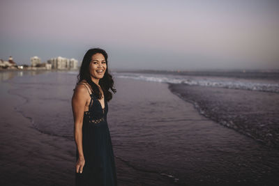 Smiling beautiful woman in long dress wading into the ocean surf