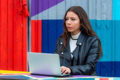 Young woman using mobile phone against wall